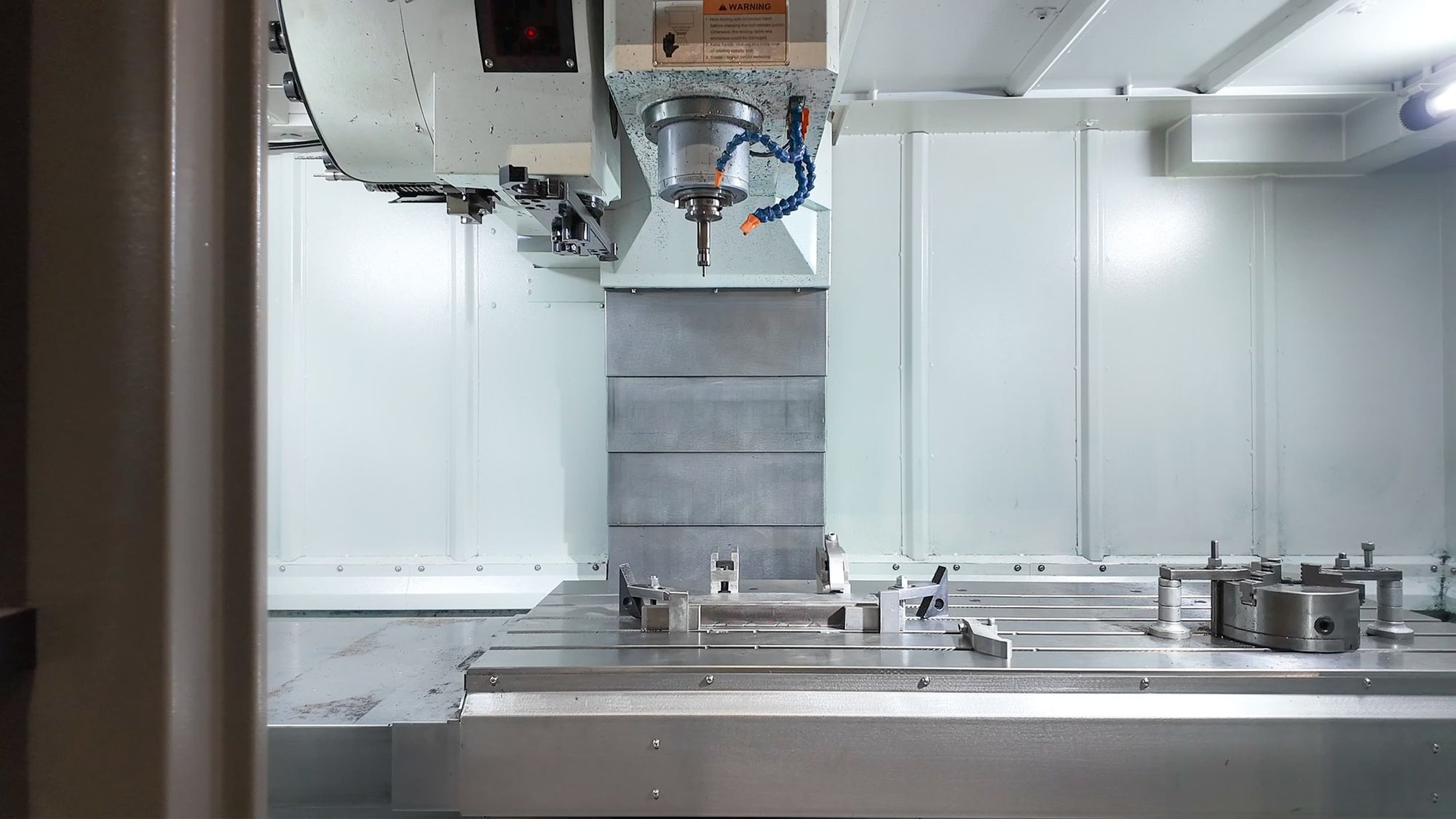 Inside a CNC machine with metal parts and a spindle ready for machining.